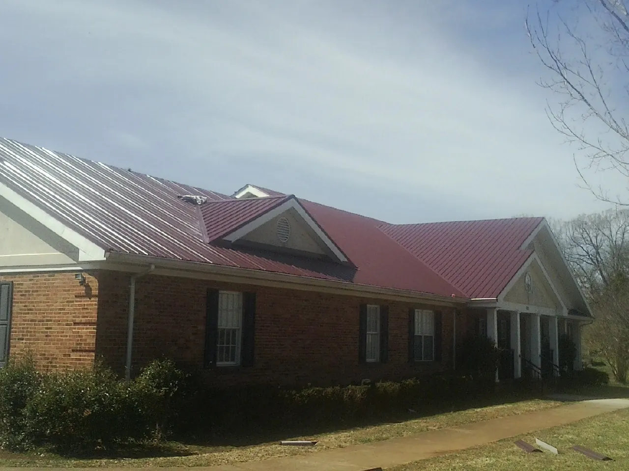 Red metal roof with gabled entries on a long brick building, from a Hail Damage Roof Repair job in Greensburg