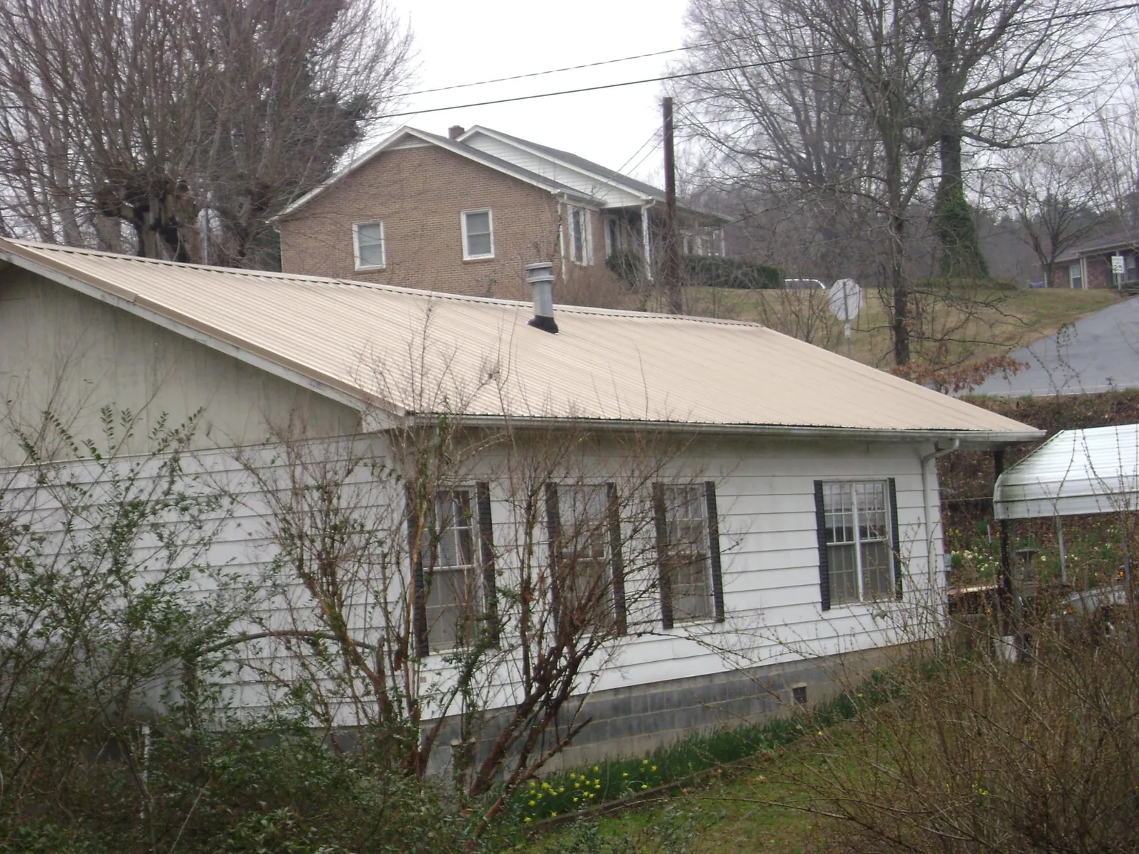 Tan metal roof on a white sided house set into a hillside — Commercial Roofing by Roofing Brothers in Greensburg