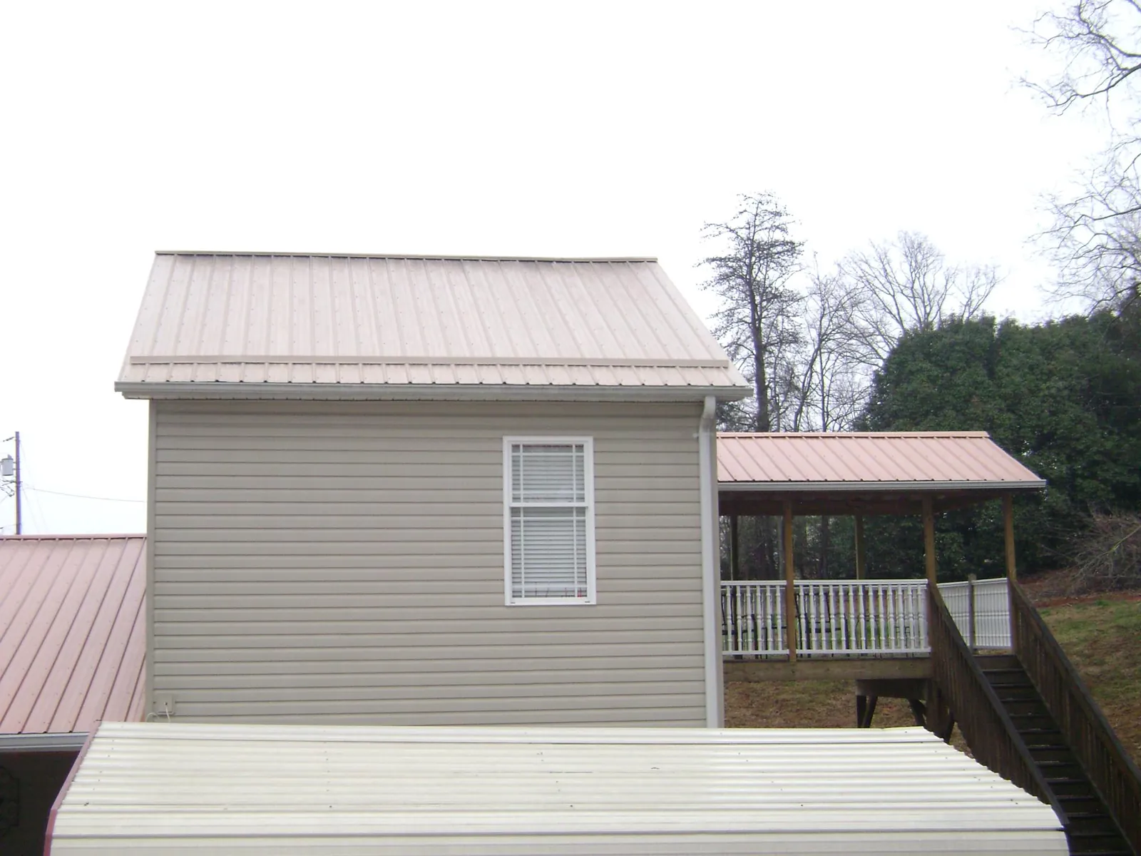 Tan metal roofs on a two story addition and attached porch, from a Roof Replacement job in Greensburg